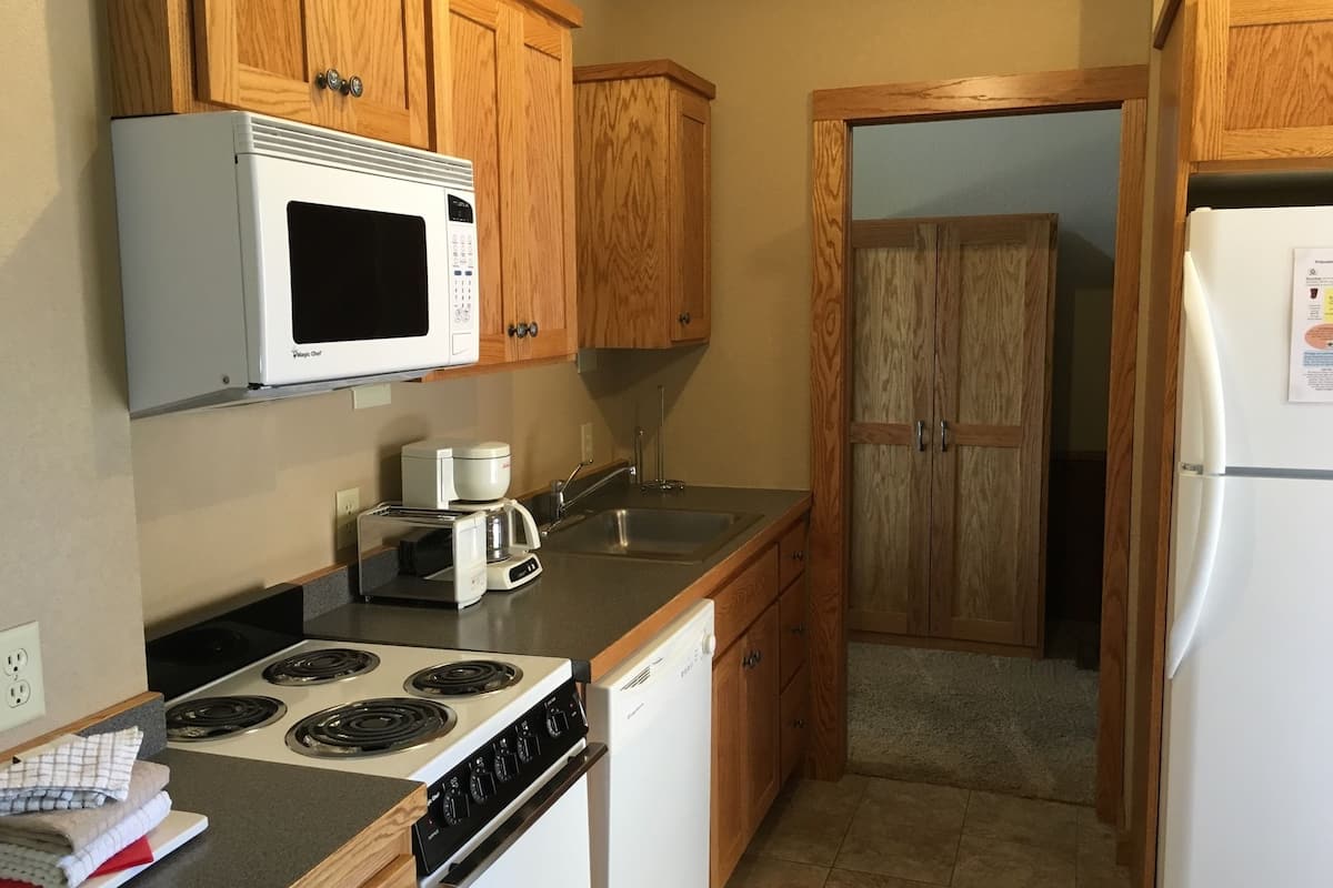 A compact kitchen with wooden cabinets, a microwave, a coffee maker, a dishwasher, and a stove.