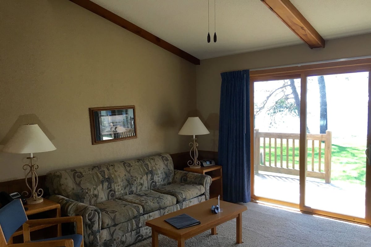 A living room with a sofa, two lamps, a coffee table, and a view of a deck.