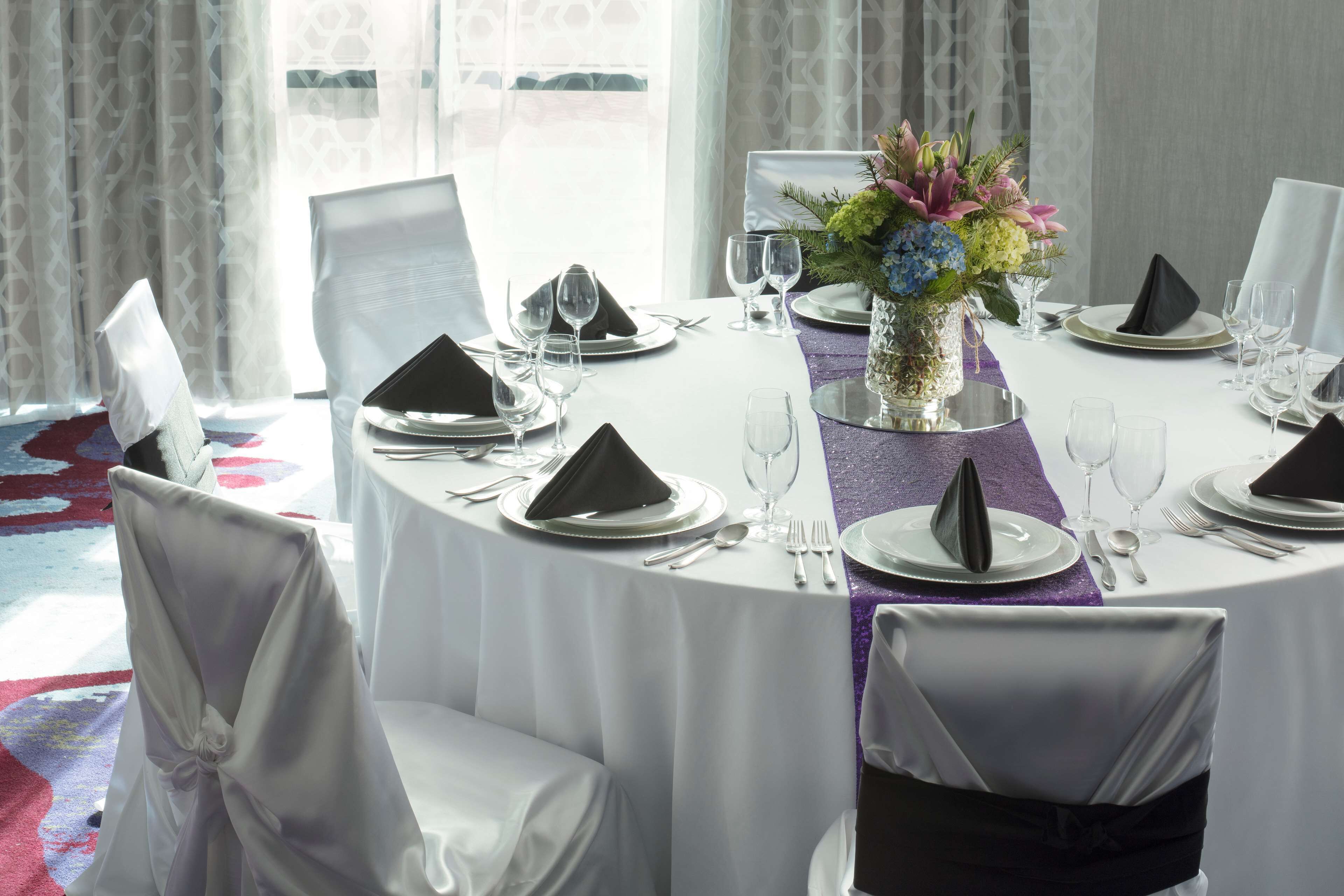 A round dining table set for a formal event with white tablecloths, black napkins, and a centerpiece of flowers.