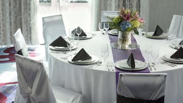 A round dining table set for a formal event with white tablecloths, black napkins, and a centerpiece of flowers.