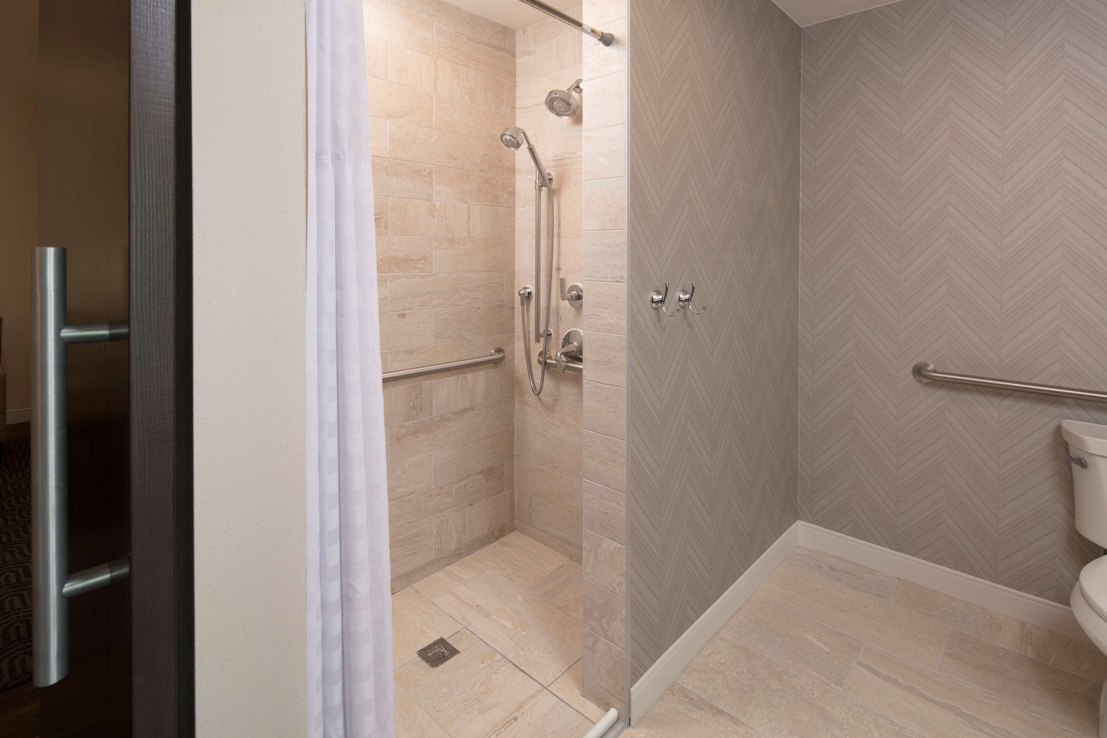 A modern bathroom with a shower, toilet, and handrails.