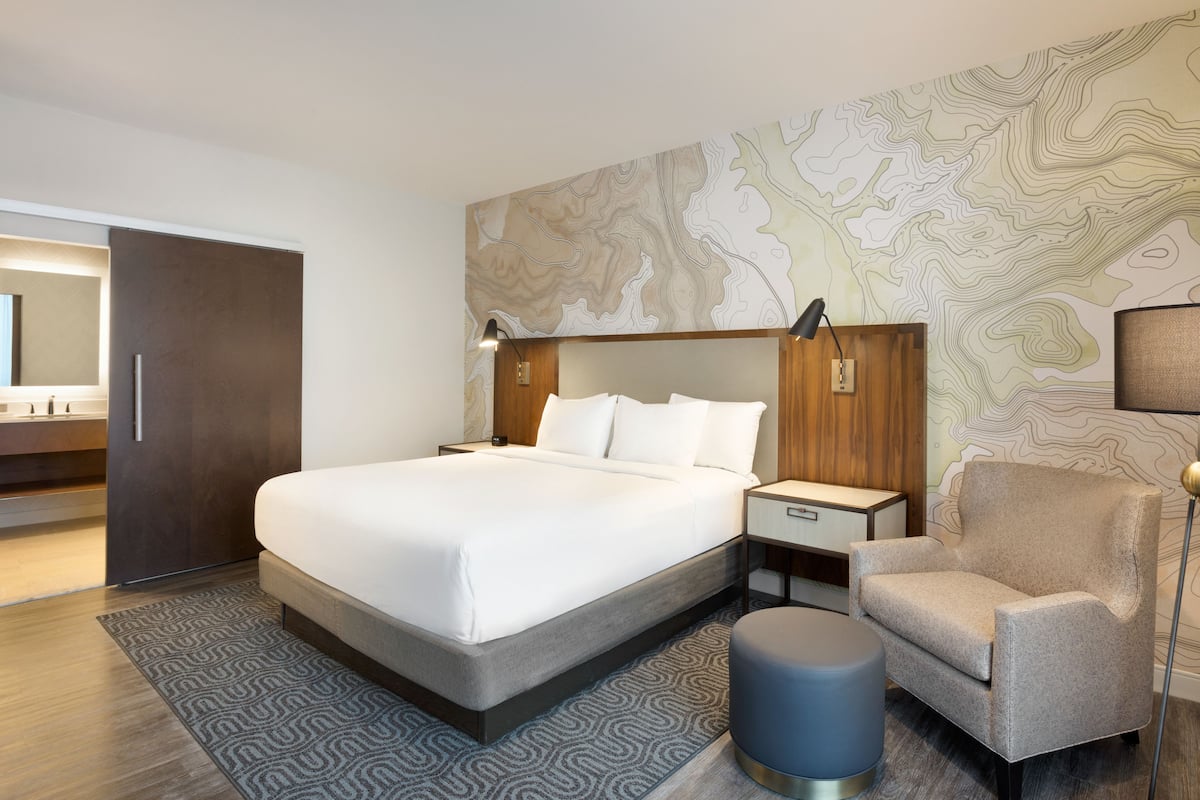 Camera d'albergo moderna con un letto grande, un comodino, una sedia e una parete con motivo di mappa topografica.