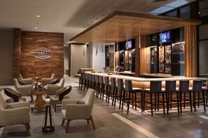 A modern bar area with a long counter, bar stools, and a wooden accent wall with a logo. - Embassy Suites by Hilton Amarillo Downtown (Amarillo)