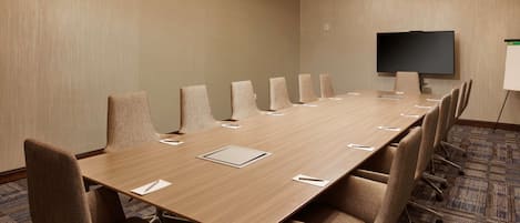 A conference room with a long table, multiple chairs, a flat-screen TV, and a whiteboard.
