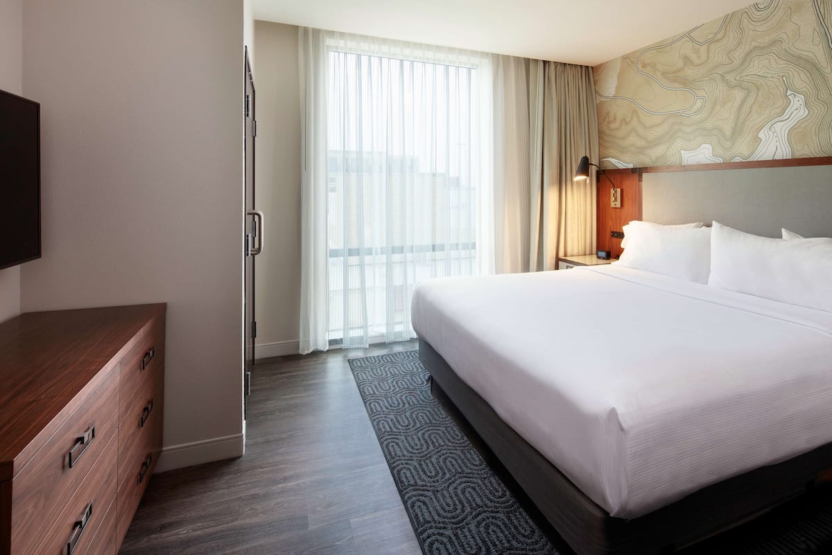 Una camera d'albergo con un letto grande, un comò in legno, una televisione a schermo piatto e una finestra con tende leggere.
