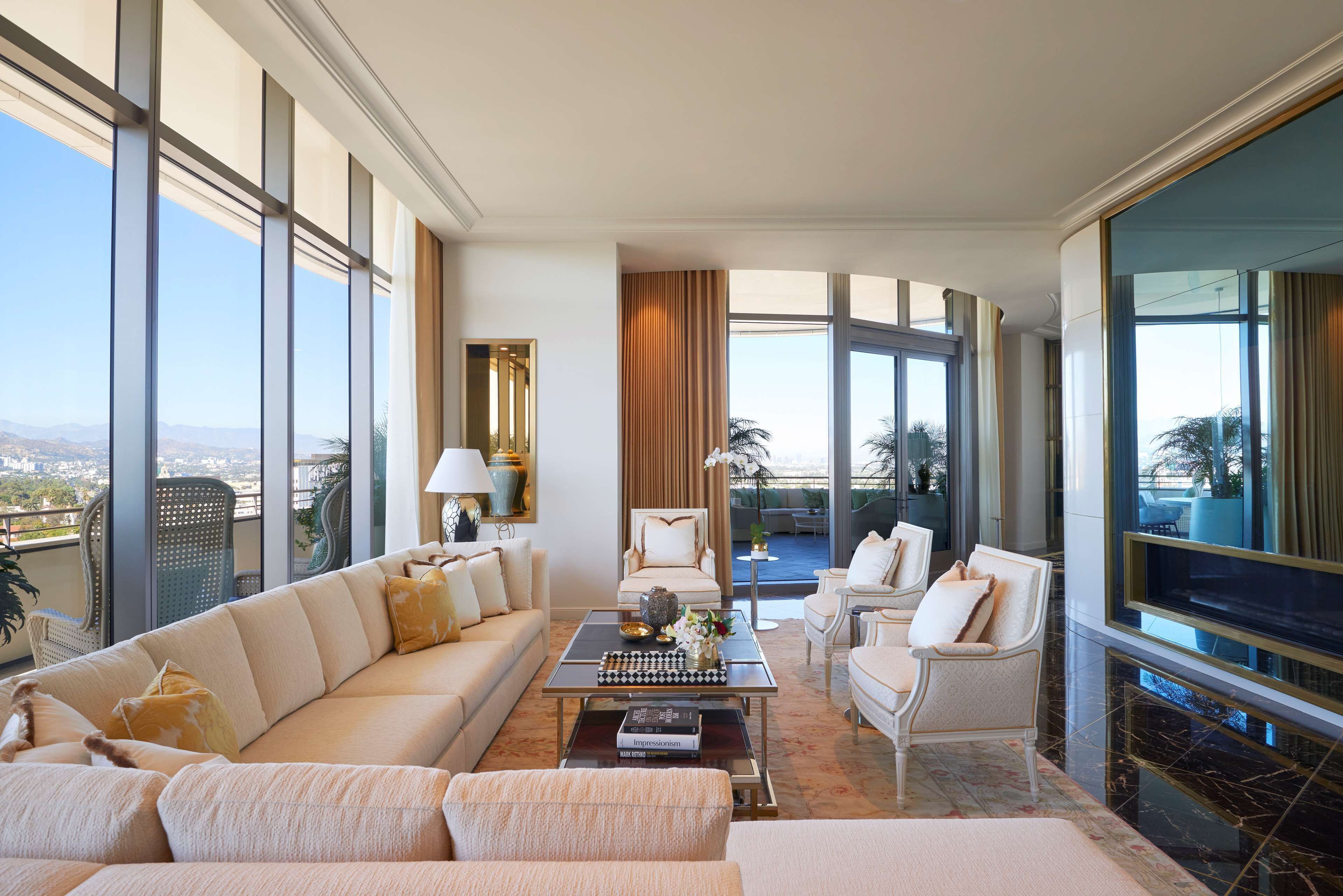 Amplia sala de estar con un sofá grande, una mesa de centro y un televisor. Amplias ventanas ofrecen vistas a la ciudad y a las montañas.