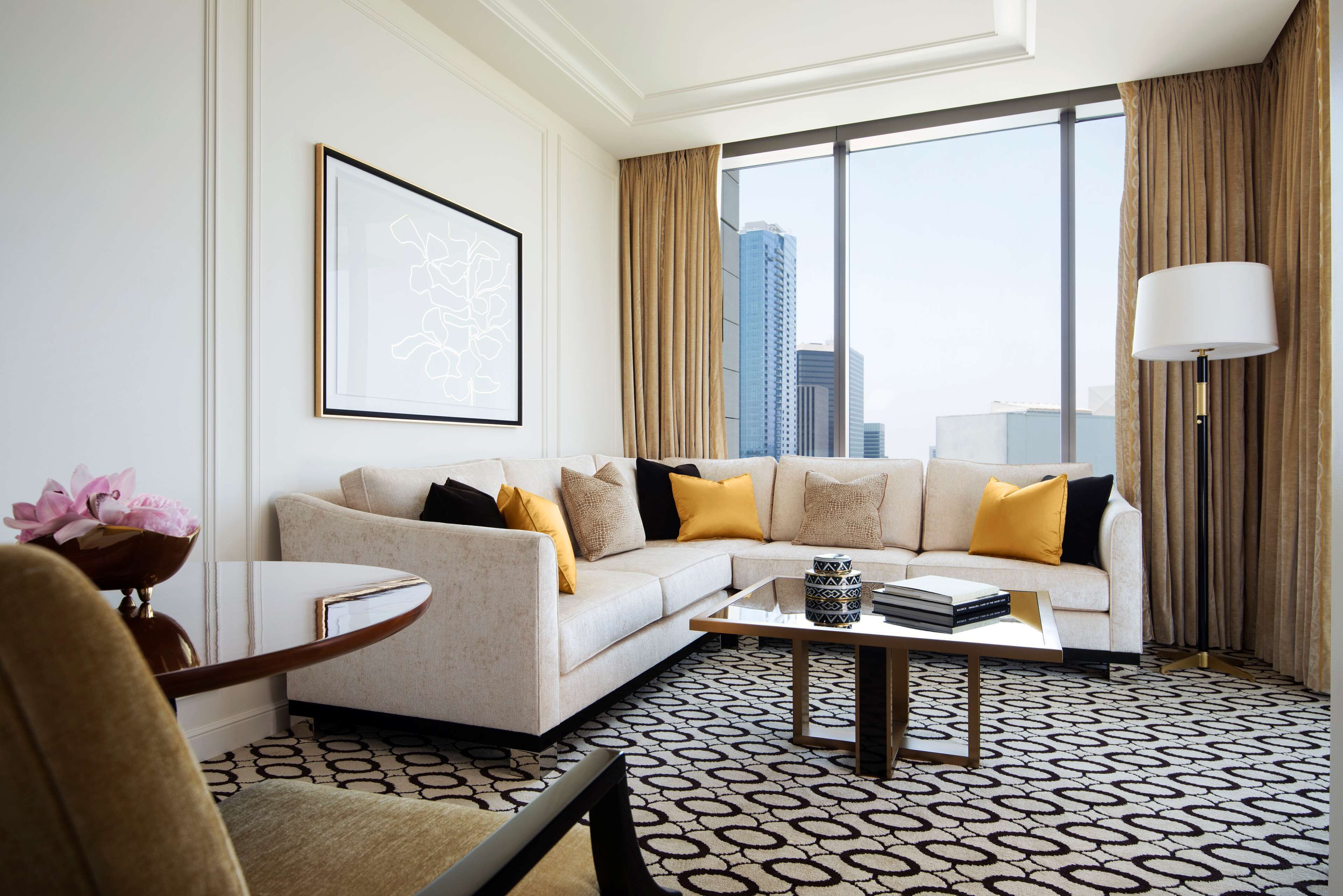 A modern hotel room with a large window, a sofa, a coffee table, and a framed picture on the wall.