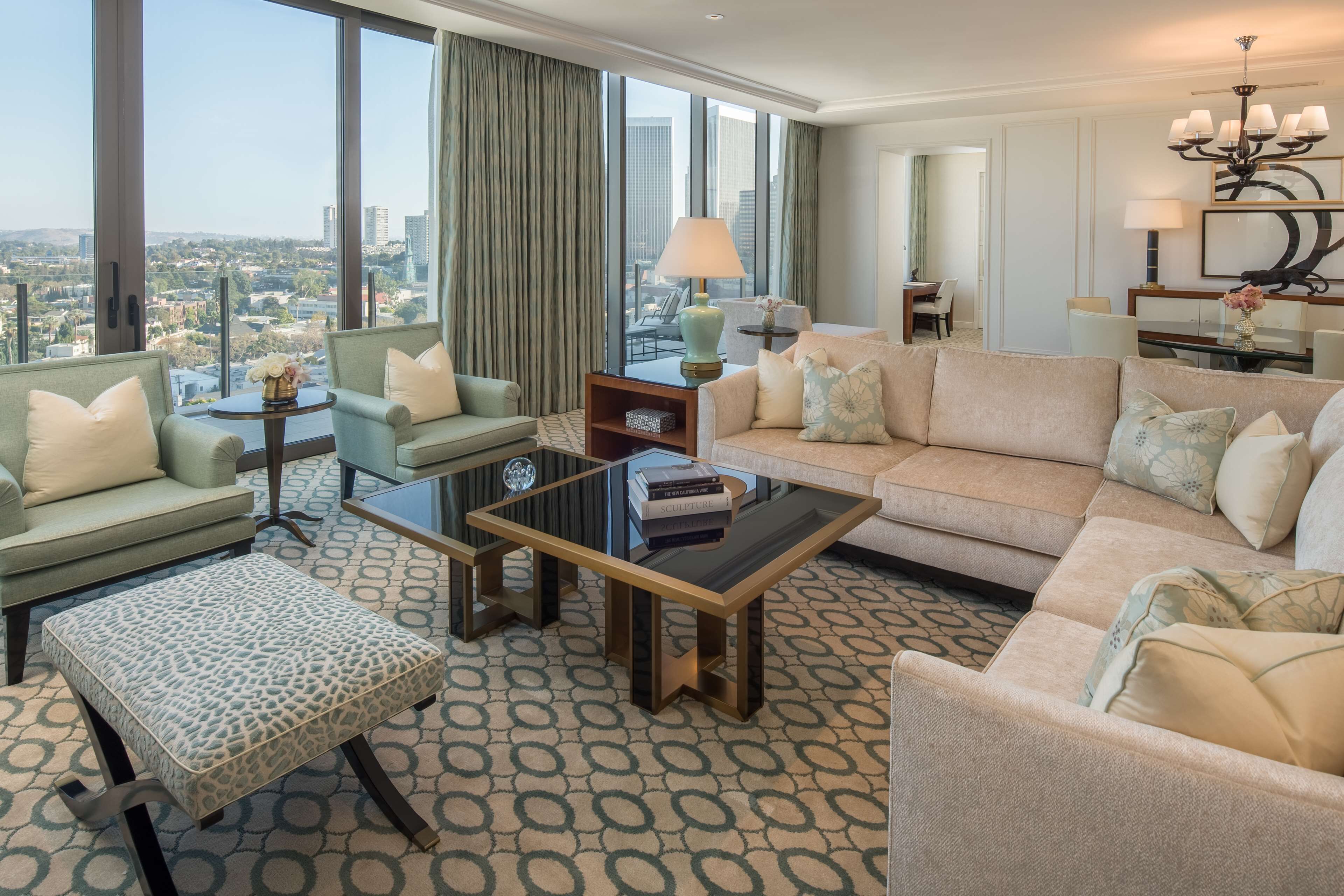 Une chambre d’hôtel moderne dotée d’une grande fenêtre donnant sur la ville, d’un canapé, d’une table basse et d’un pouf à motifs.