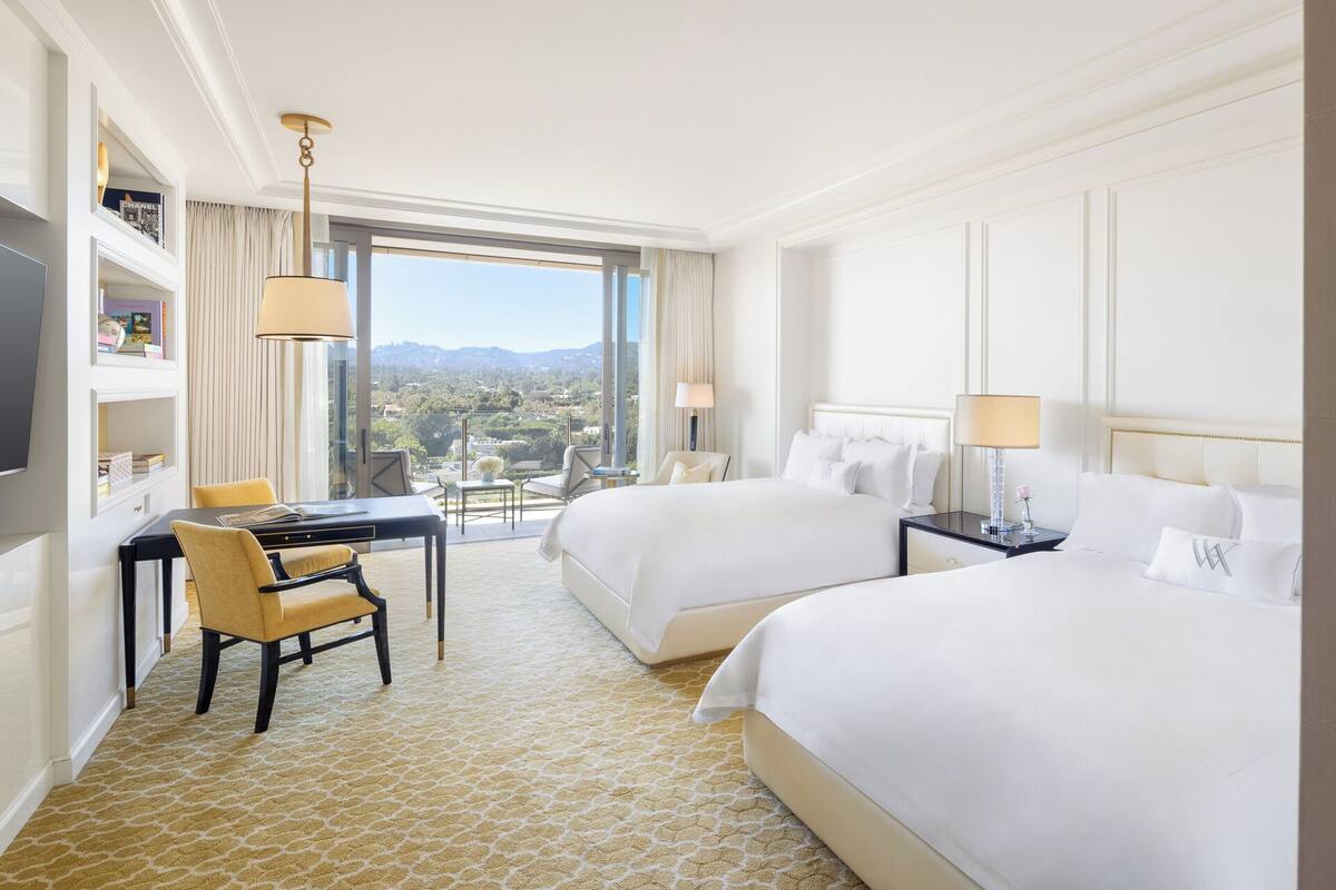 Une chambre d’hôtel avec deux lits, un bureau et une chaise, une télévision et une vue sur la ville.