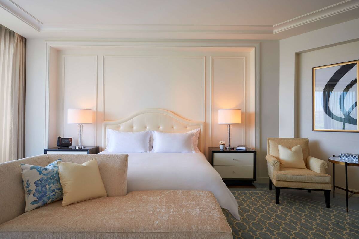 Une chambre d’hôtel avec un grand lit, deux tables de chevet, une chaise, un canapé et une œuvre d’art encadrée au mur.