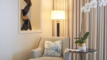 A hotel room with a grey armchair, a round table with a potted orchid, a lamp, and a large mirror on the wall.