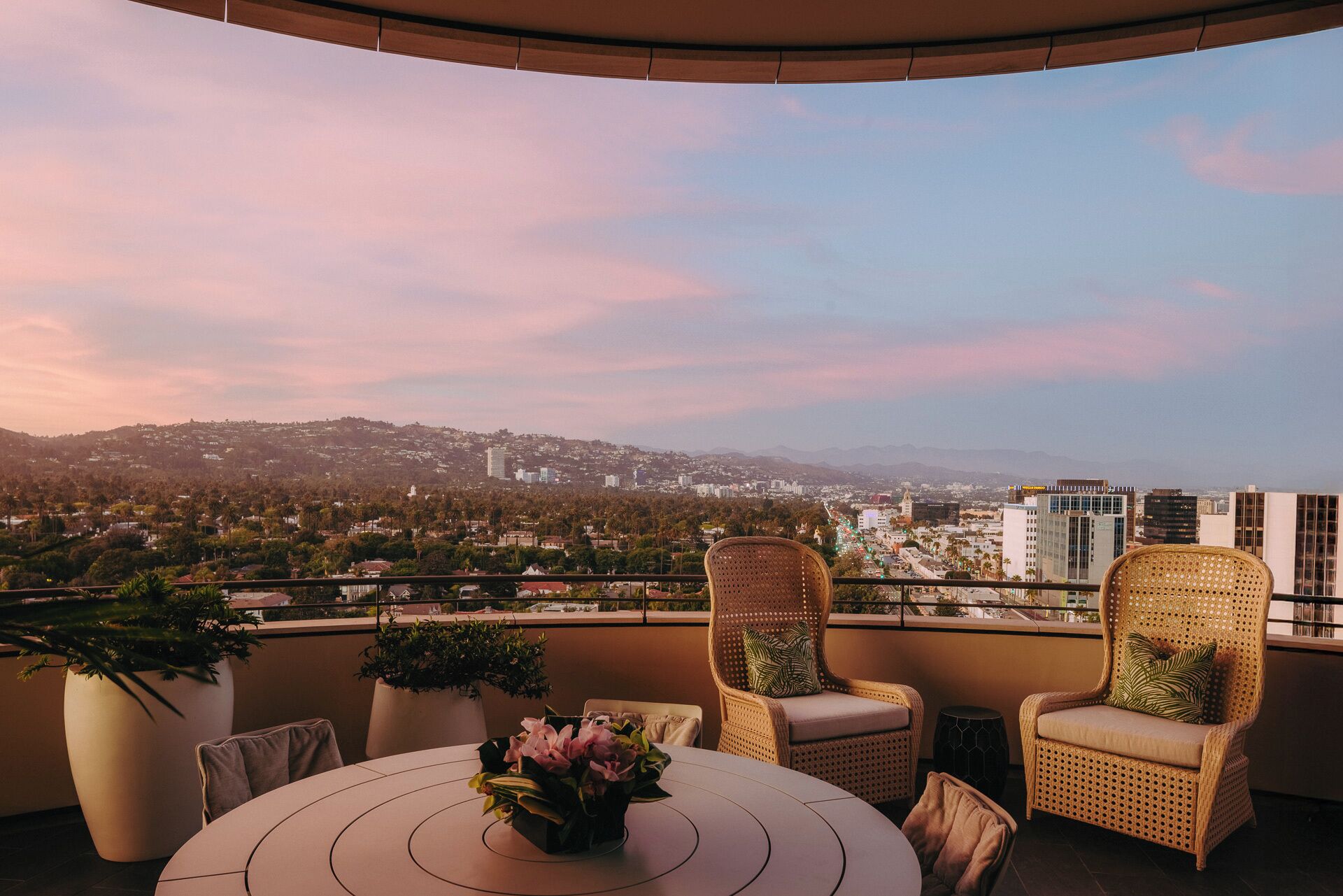 A balcony with wicker chairs, a round table, and a vase of flowers.