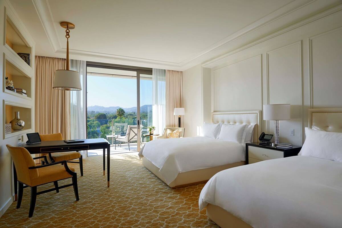 Une chambre d’hôtel avec deux lits, un bureau avec un ordinateur portable, une chaise, une table de chevet avec un téléphone et une vue sur l’extérieur.