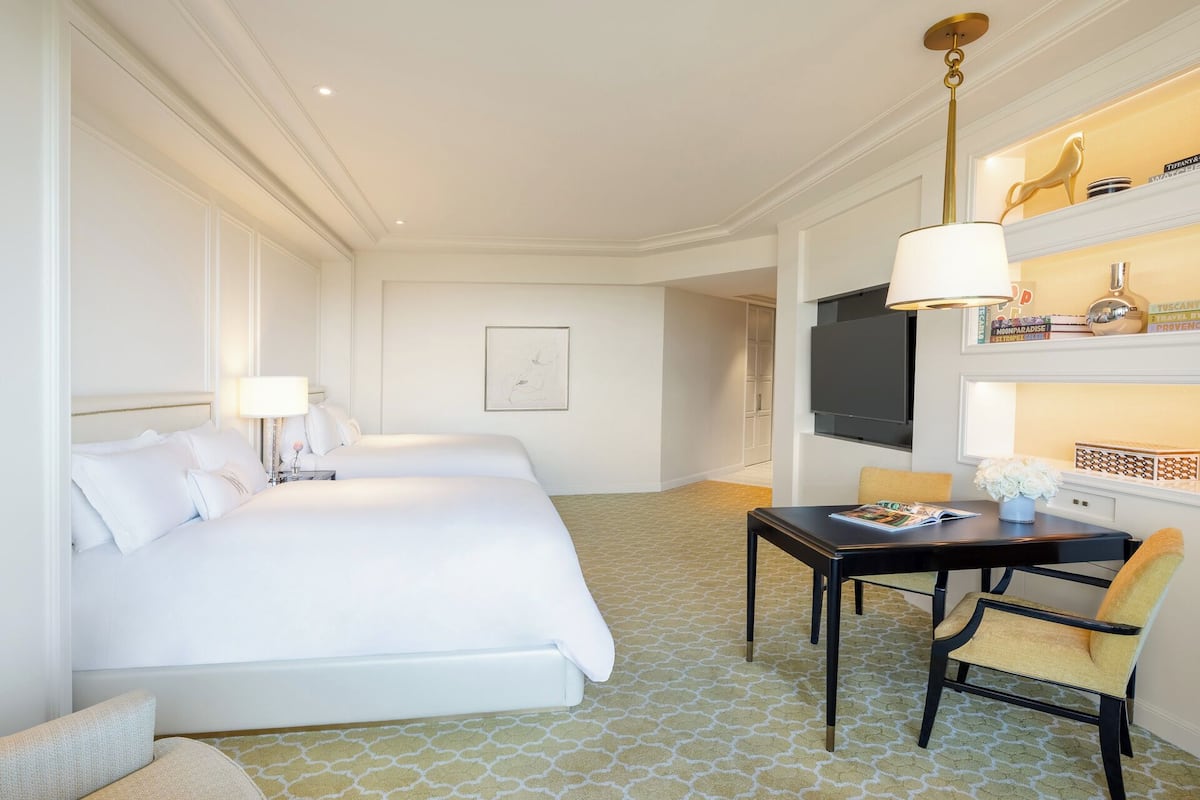 Une chambre d’hôtel avec un grand lit, un bureau avec une chaise, une télévision et une bibliothèque contenant des livres et des objets de décoration.