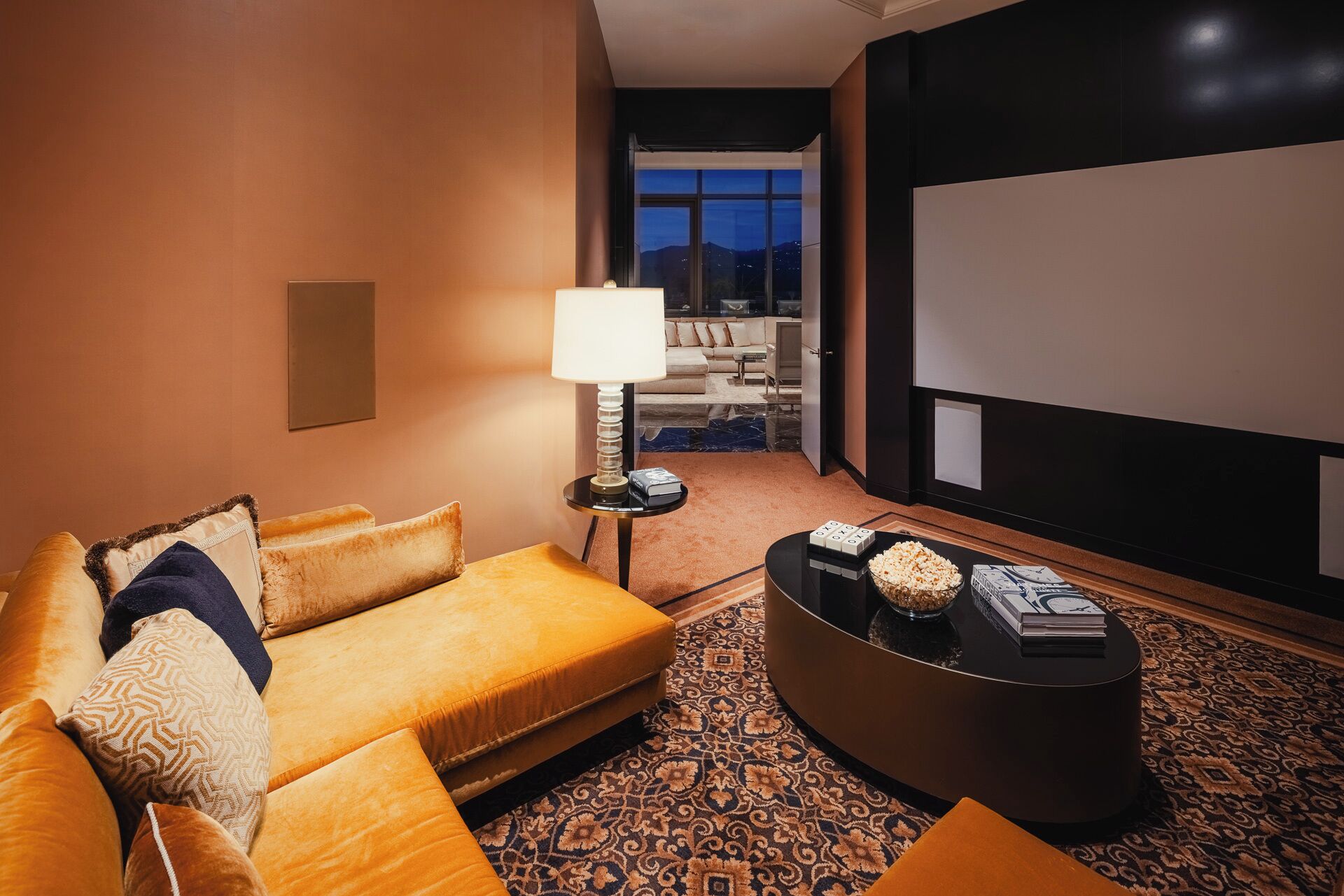 A hotel room with a sofa, a coffee table, a lamp, a large window, and a television.