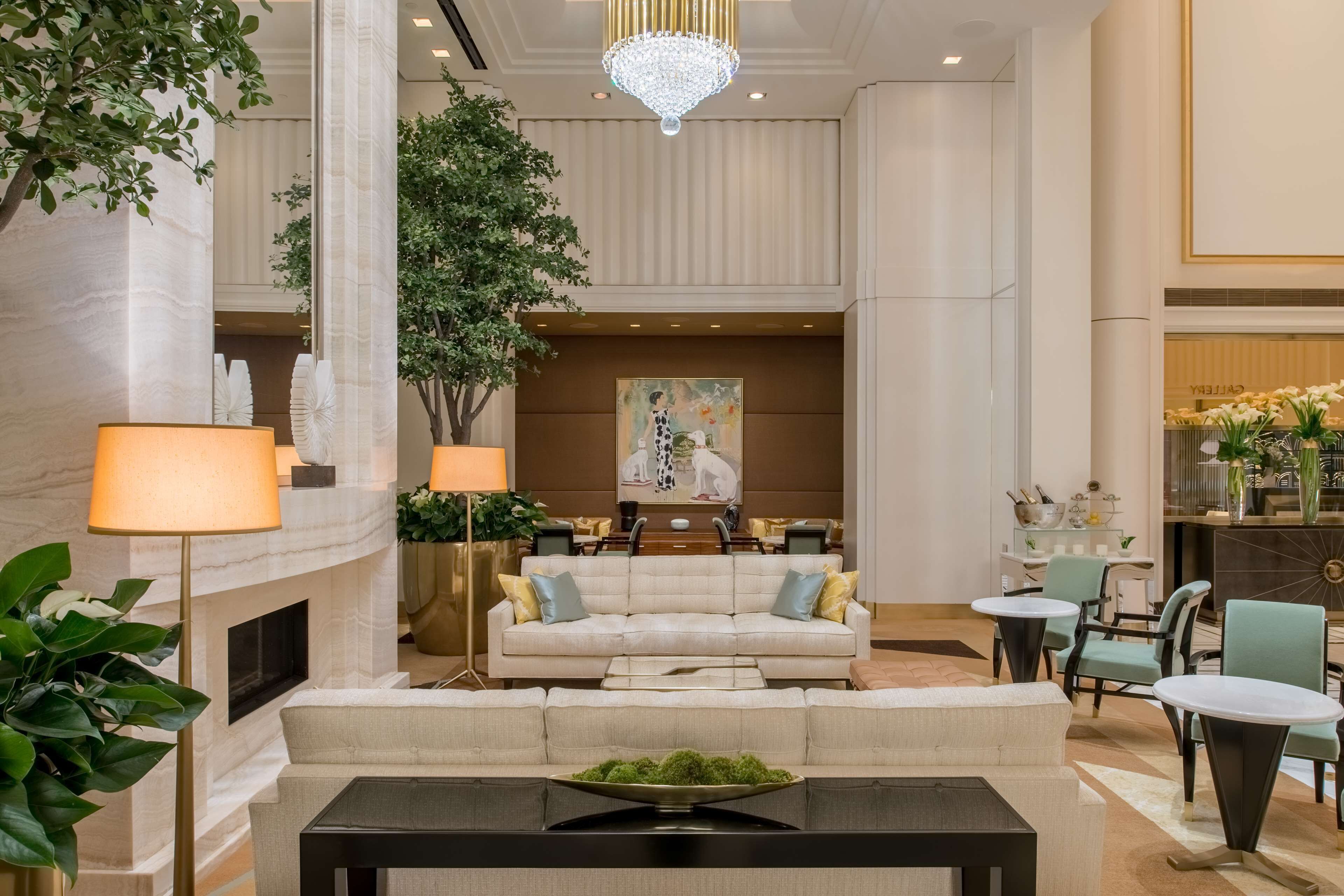 A spacious lobby with a high ceiling, a chandelier, a fireplace, a seating area with a sofa and chairs, and a dining area with tables and chairs.