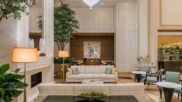 A spacious lobby with a high ceiling, a chandelier, a fireplace, a seating area with a sofa and chairs, and a dining area with tables and chairs.