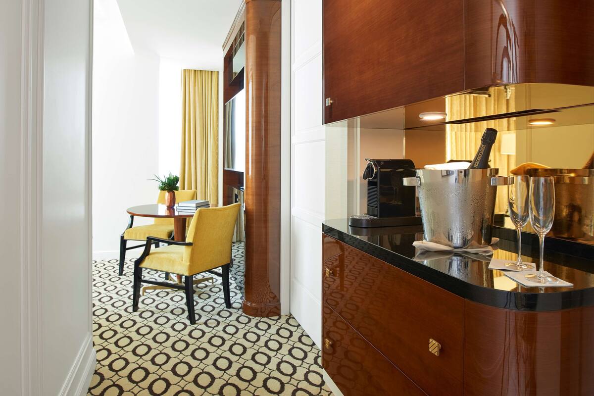 Une chambre d’hôtel avec un meuble en bois, un coin repas avec une chaise jaune et un sol à motifs.