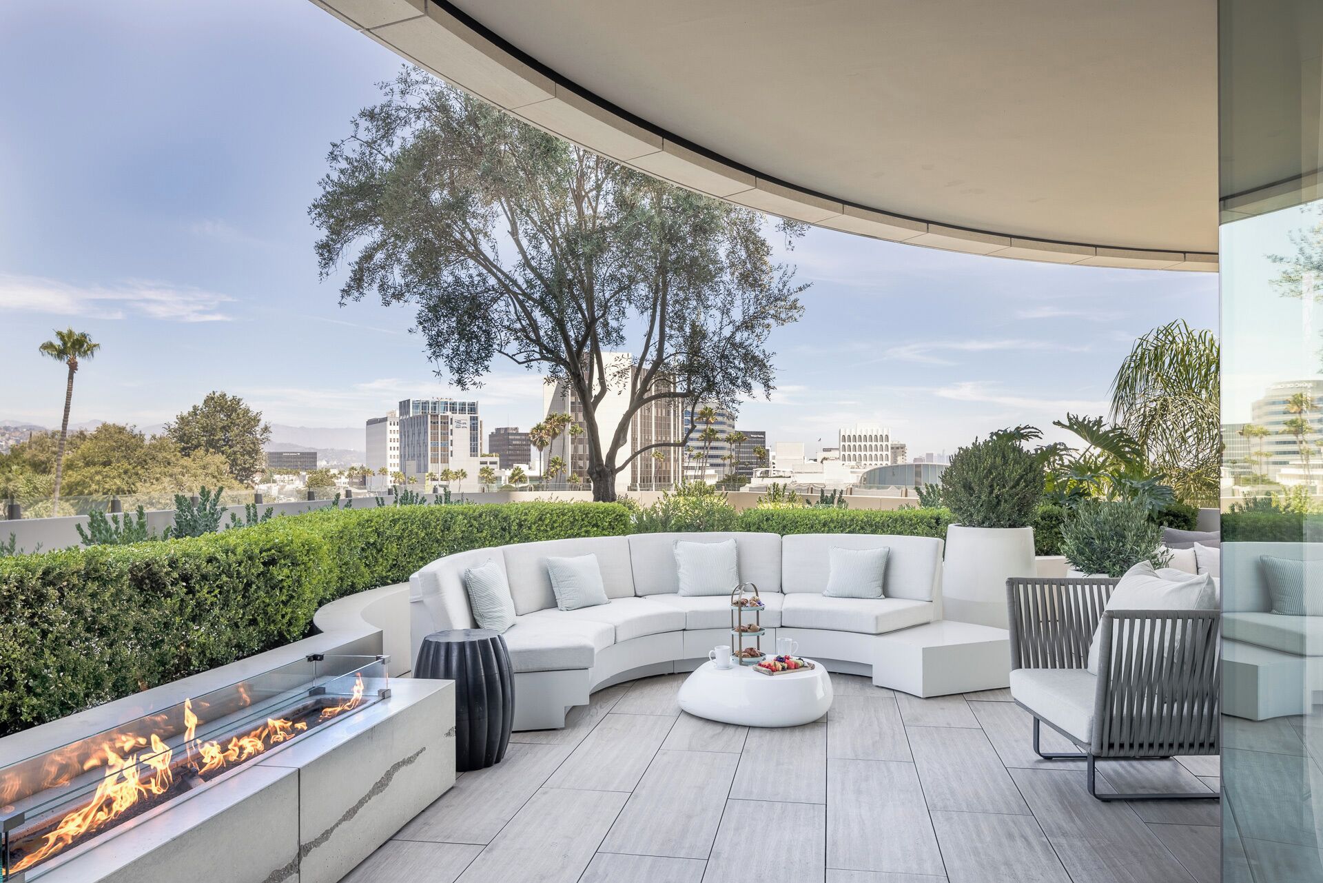 A modern outdoor seating area with a fire feature, a tiered serving tray, and a city view.