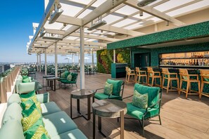A rooftop bar with green seating, a bar area, and a city view.