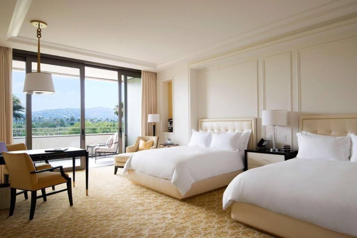 Une chambre d’hôtel avec deux lits, un bureau, une chaise et une vue sur l’extérieur.