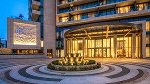 Une entrée d’hôtel moderne, agrémentée d’une fontaine circulaire et dotée d’une grande façade illuminée.