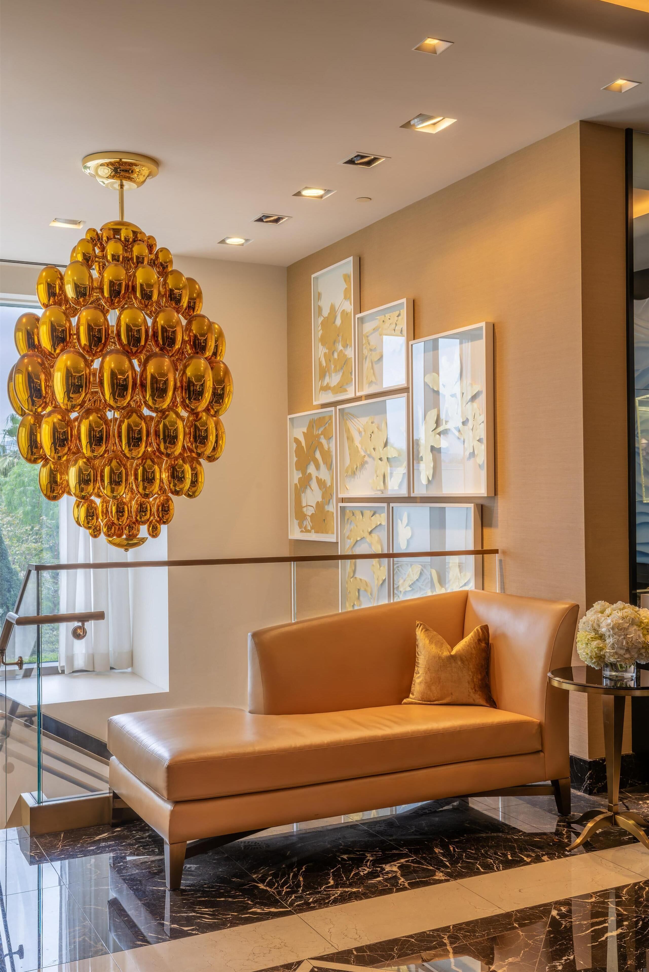 A modern lobby with a leather sofa, a unique golden chandelier, and framed artwork on the wall.