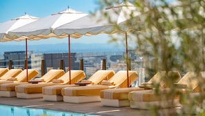 Un espace aménagé au bord de la piscine, avec des chaises longues et des parasols, offrant une vue dégagée sur le paysage urbain en arrière-plan.