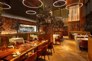 A restaurant with wooden tables, green booths, and a view of the kitchen.