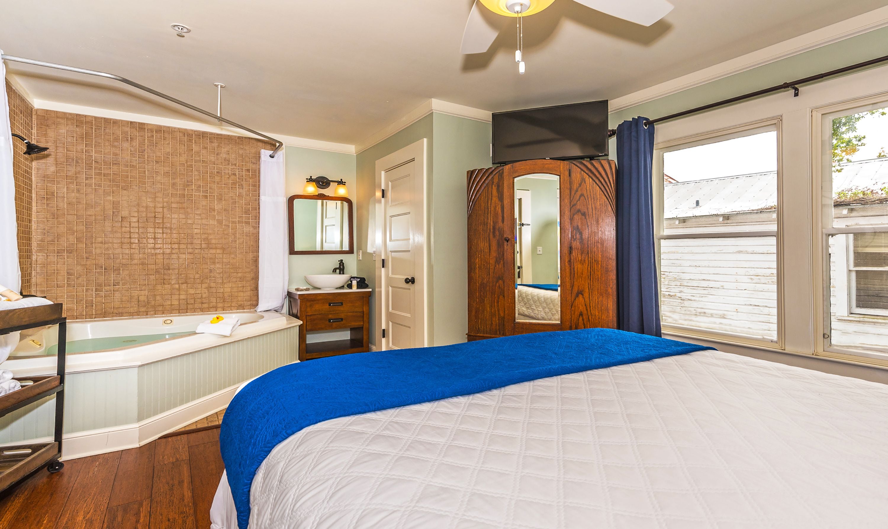 Ein Schlafzimmer mit einem großen Bett, einer Badewanne, einem Schminktisch mit Spiegel und einem Fenster mit Blick nach draußen.