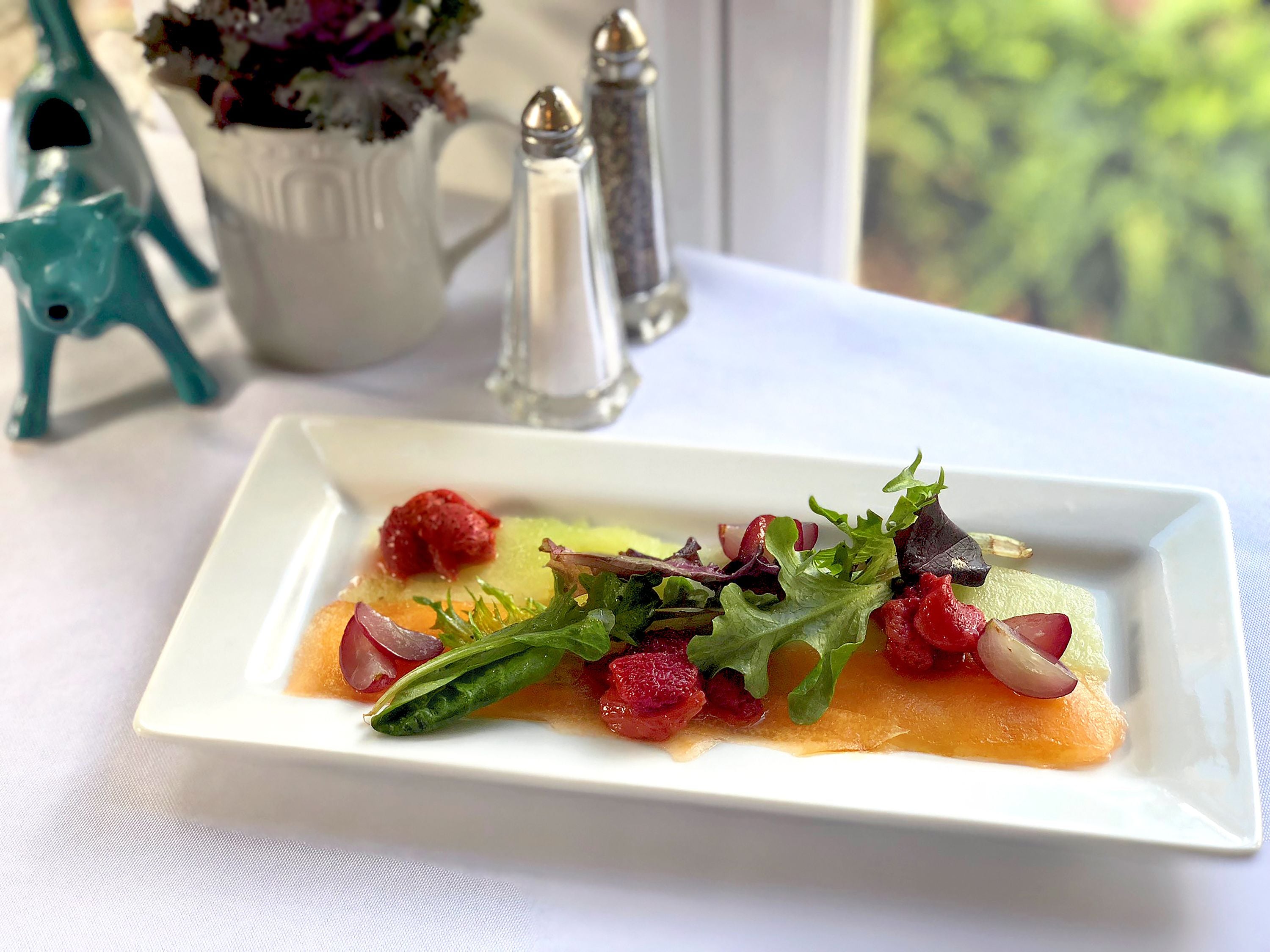 A white rectangular plate with a salad on a white tablecloth.