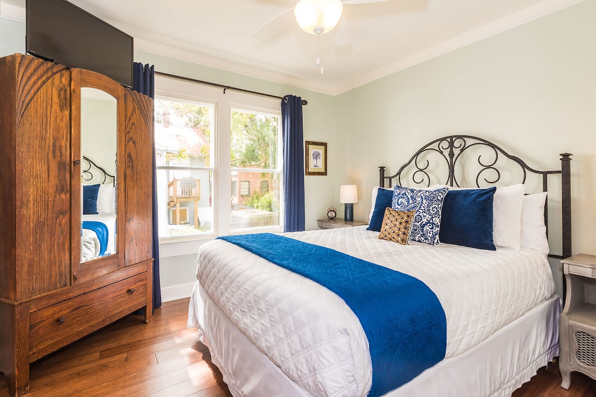 A bedroom with a large bed, a wooden wardrobe, a nightstand, and a window with curtains.