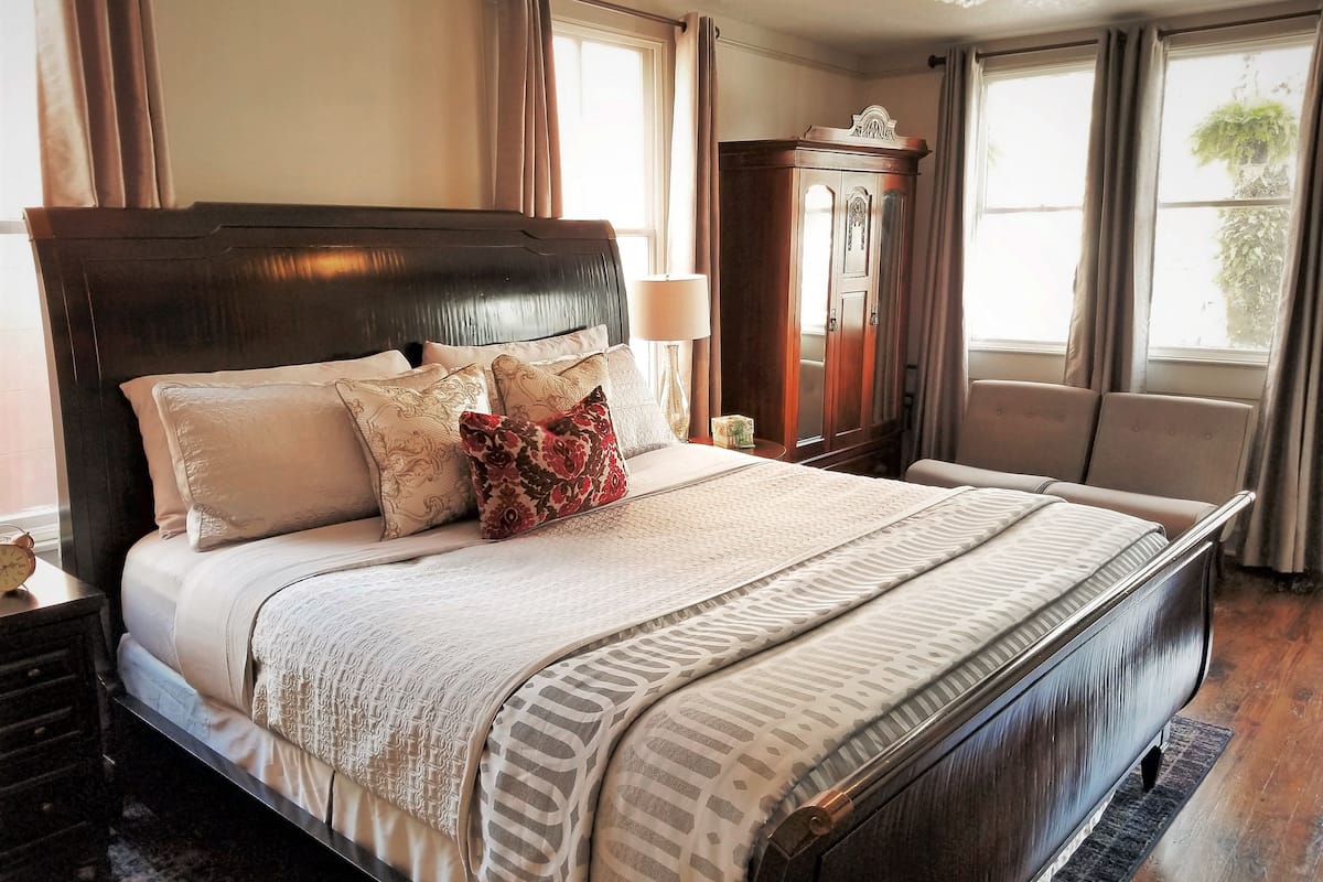 A large bed with multiple pillows, a wooden wardrobe, and a nightstand with a lamp.