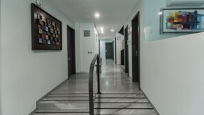 Un pasillo moderno de hotel con piso de mármol, obras de arte enmarcadas en las paredes y una vitrina de vidrio.