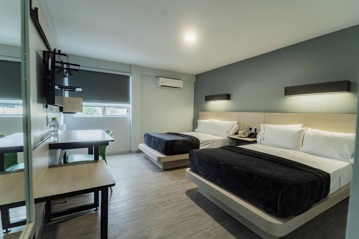 Habitación de hotel moderna con una cama grande, un escritorio y una silla. Cuenta con una ventana que ofrece luz natural y vistas al exterior.