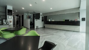 Un lobby moderno de hotel con una mesa de recepción, sillas verdes y una mesa negra.
