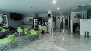 Un moderno vestíbulo de hotel con recepción, cocina y comedor con sillas verdes.