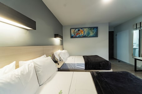 A hotel room with two beds, a painting on the wall, and a desk with a lamp.