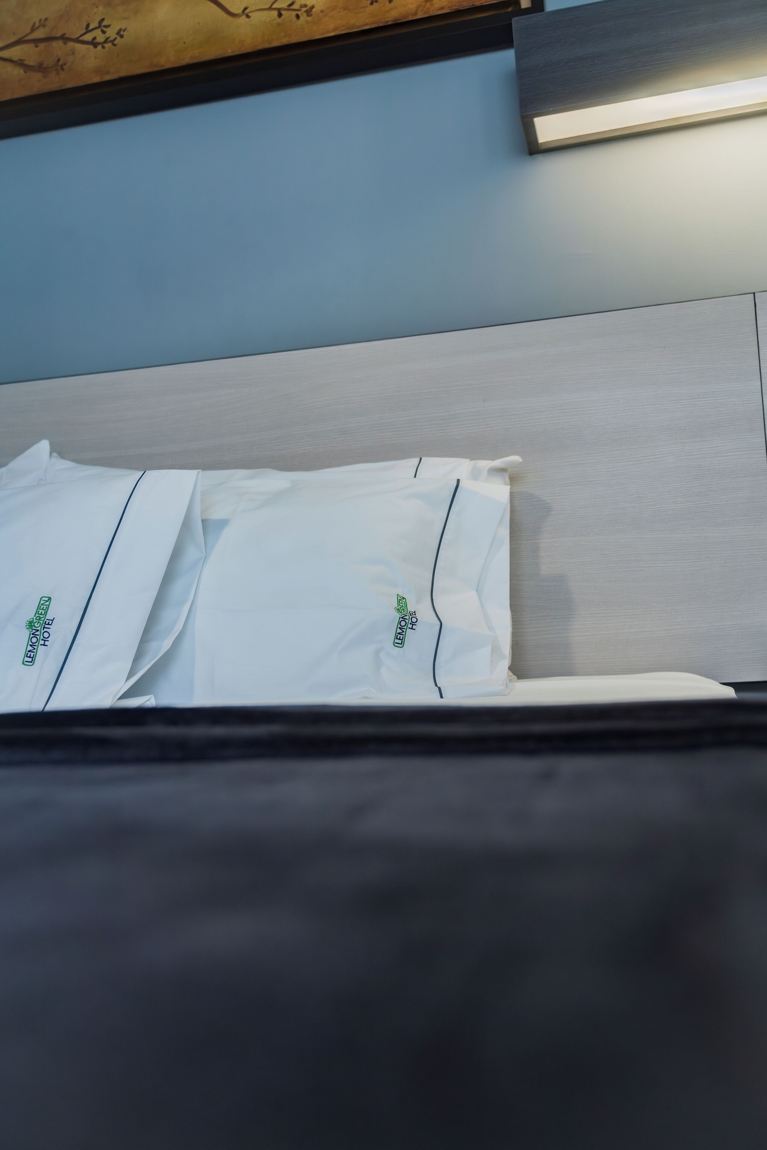 A neatly made bed with white linens and green text, a light blue wall, and a wooden headboard.