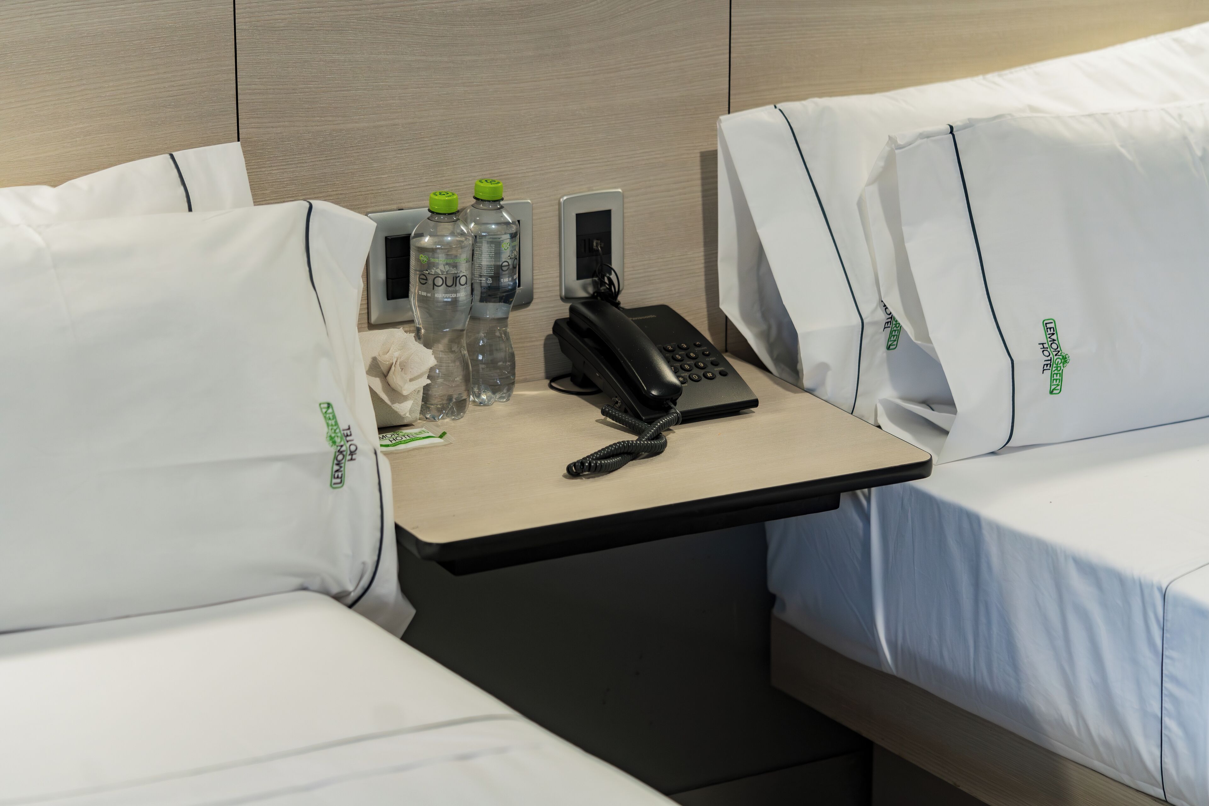 A hotel room with two beds, a small table with a phone, two water bottles, and a tissue box.