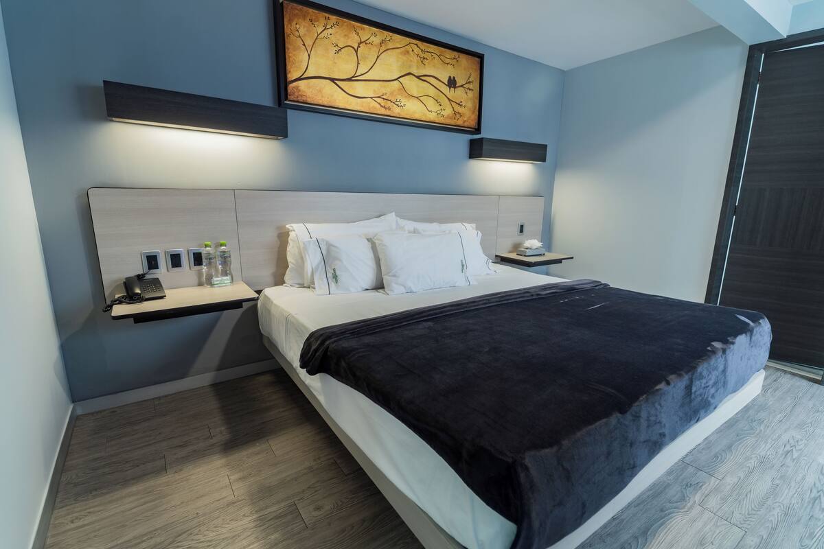 Un dormitorio moderno con una cama grande, mesitas de noche, una obra de arte en la pared y un estante empotrado con artículos de tocador.