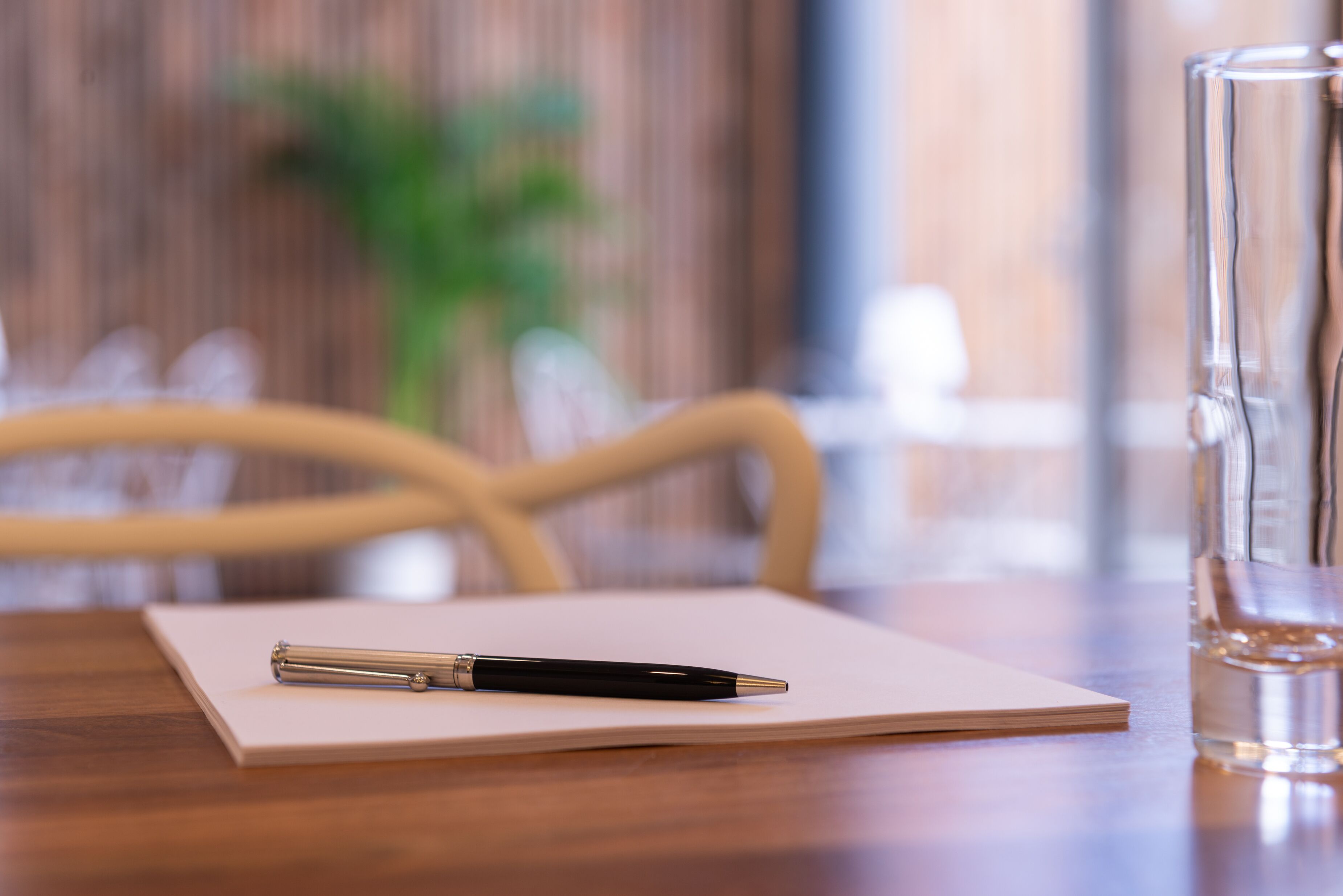A wooden table with a notebook, a pen, and a glass of water.