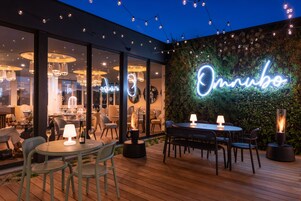 Uma área de refeições ao ar livre com mesas, cadeiras, um letreiro de neon e luzes de Natal.