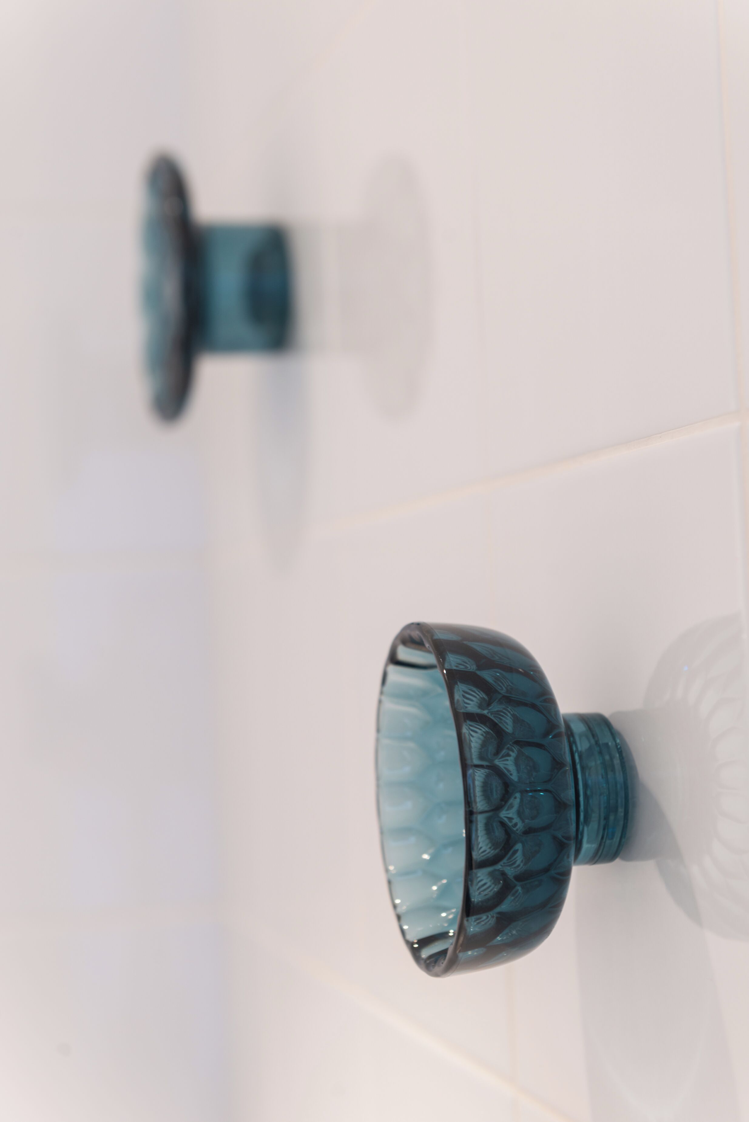 A bathroom with a white tiled floor, a blue glass showerhead, and a blue glass basin.