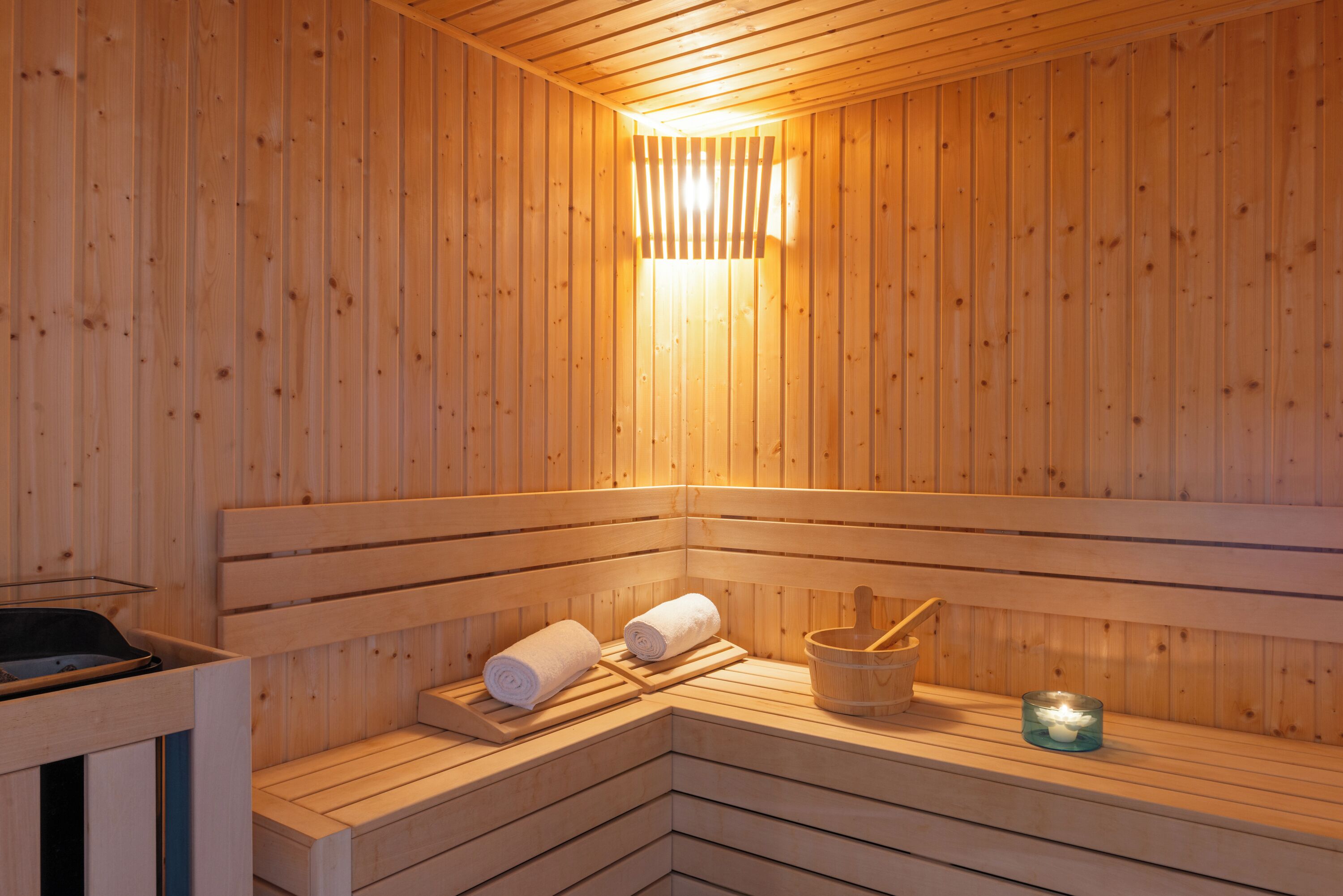 A wooden sauna with benches, a towel, a bucket, and a candle.