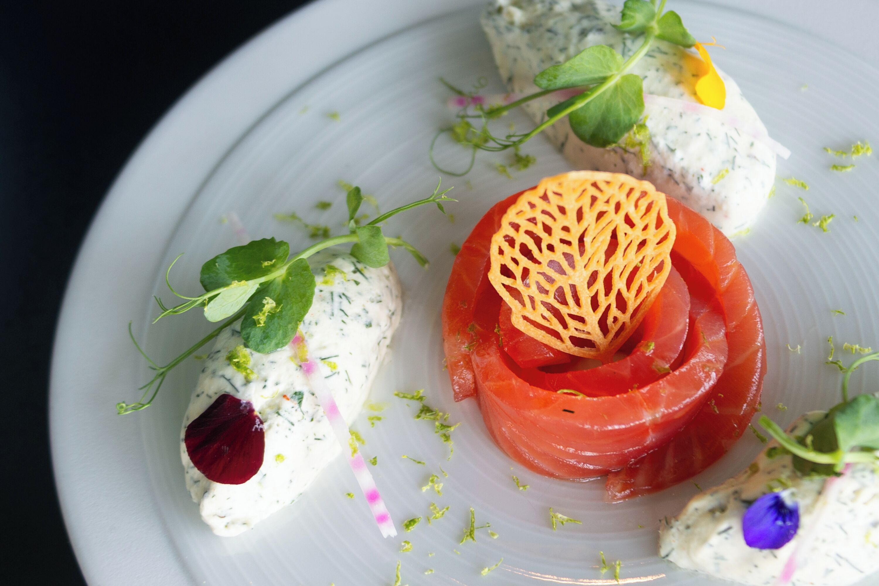 Un plato blanco con alimentos, incluyendo una porción de salmón, una remolacha y un adorno.