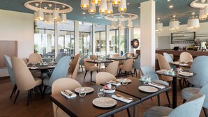 Un intérieur de restaurant moderne, avec de nombreuses tables, des chaises et des luminaires suspendus.