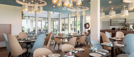 A modern restaurant interior with multiple dining tables, chairs, and pendant lighting.