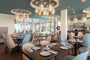 Interior moderno de restaurante com várias mesas, cadeiras e iluminação pendente.