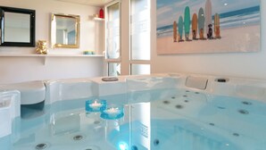 Un espace détente avec un grand jacuzzi, une peinture représentant des planches de surf sur le mur et un ours en peluche sur une étagère.